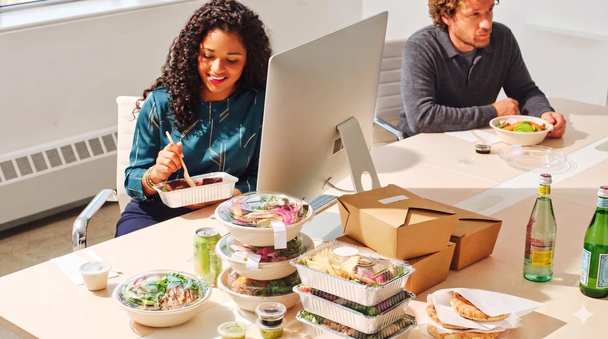 Colleagues eating individually ordered restaurant meals at their desks in a London office